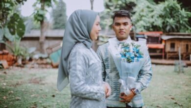 A Muslim couple in traditional attire shares a moment outdoors with a floral bouquet.